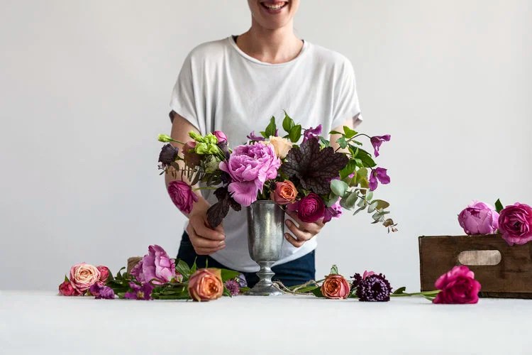 Person arranging a colorful flower bouquet on a white table.